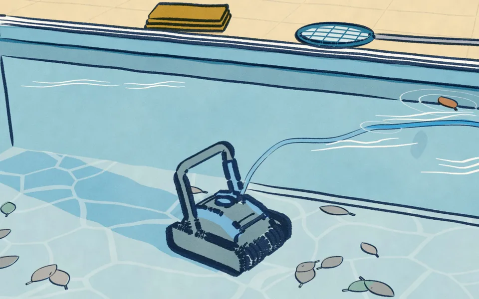 A pool robot on the floor of a swimming pool, seen through the water, a clean path behind it through sunk leaves, a leaf net and a folded towel on the deck.