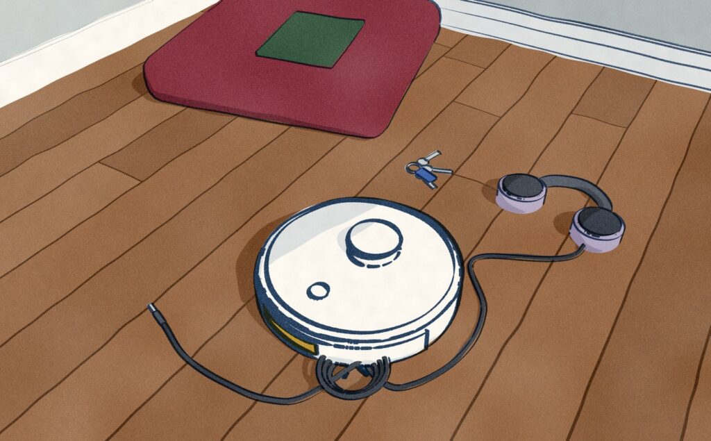 In the reading corner of the same playroom, the white Roborock Qrevo MaxV has stopped with a headphone cable wound round its side brush; the headphones lie on the floor behind it where it dragged them off the floor cushion, the jack trails ahead, and a set of keys lies flat in its track where it ran over them.