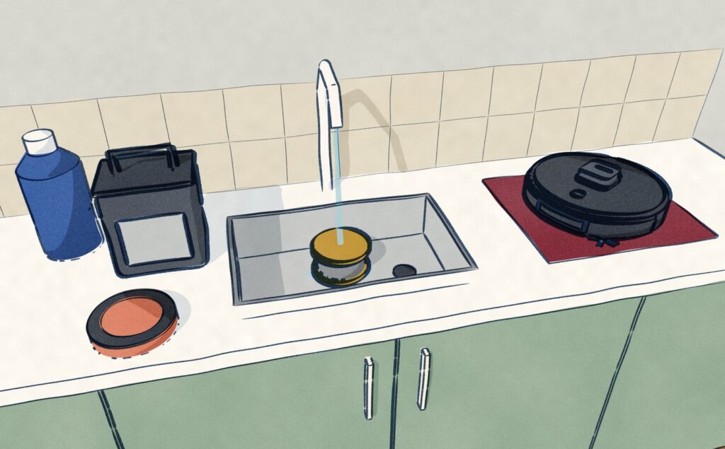 At the kitchen sink the Shark dock's grey-water tank stands emptied and its mesh filter sits under the running tap, a bottle of cleaner on one side and the black Shark PowerDetect lifted onto a tea towel on the other.