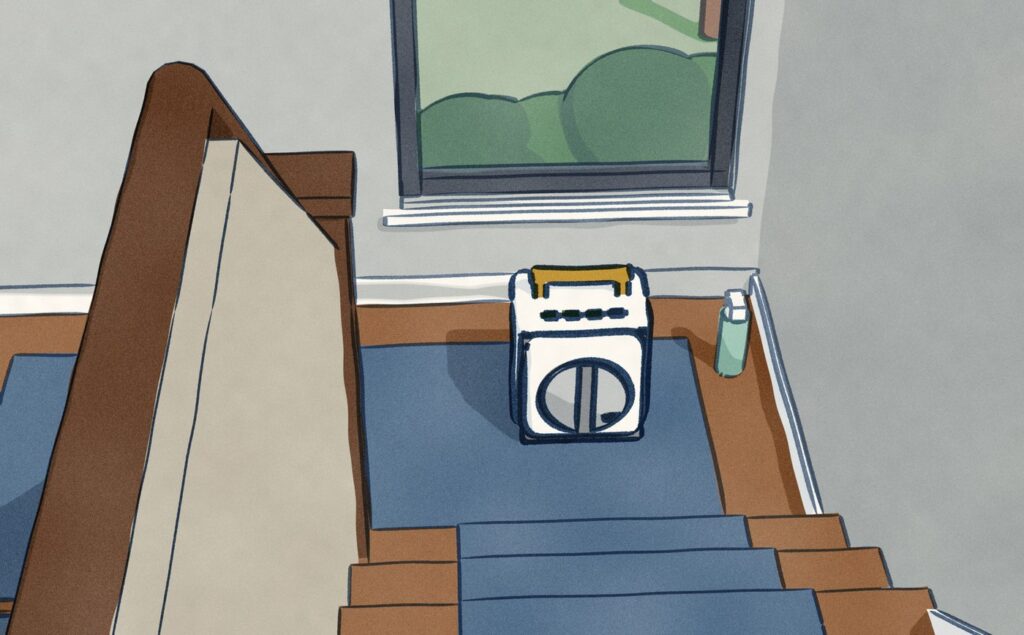 Seen from the top of a staircase, the Ecovacs Winbot W2S Pro Omni sits docked on the front of its battery station, set down on the half-landing beneath a tall landing window with no outlet near it, a spray bottle beside it.