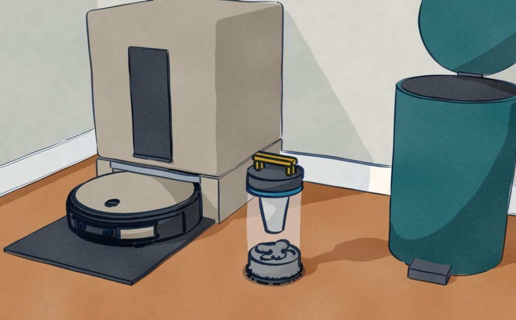 In a hall alcove, the black Ecovacs X12S sits charging in its warm grey dock while the dock's clear cyclone dust canister, lifted out of its slot, stands on the tiles beside an open pedal bin.