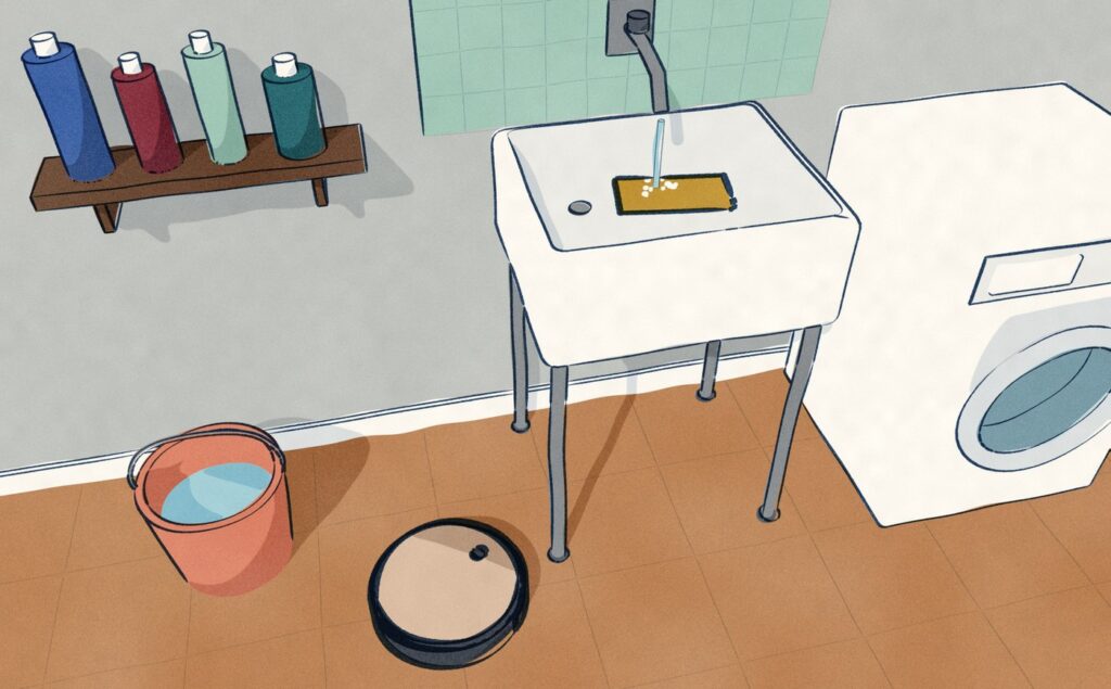 In a utility room the Roomba Combo j9+'s mop pad lies under the running tap in a deep tub to be washed by hand, while the robot waits on the tiles below without it.