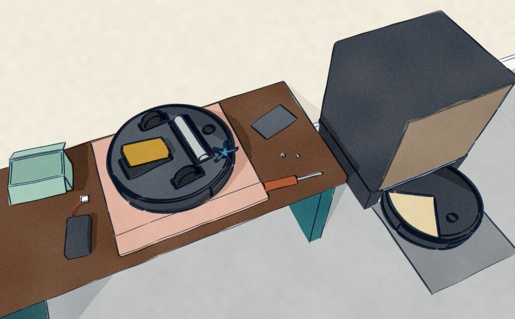 On a hall bench a black robot vacuum lies upside down on a folded tea towel with its battery door off: the old battery pack lies on the bench beside the door and its two screws, a new pack is going into the bay, and beyond the bench the other robot sits in its wood-fronted dock.