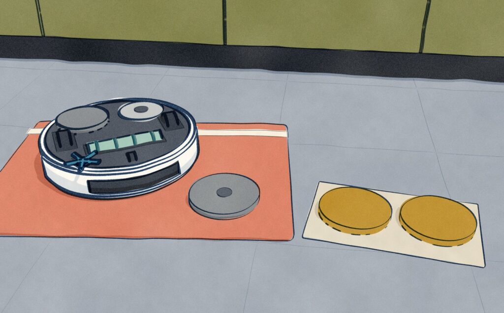 On a kitchen floor a white Dreame X50 Ultra lies upside down on a folded towel, one worn grey mop pad still on and the other off beside it, with a new pair of pads waiting.