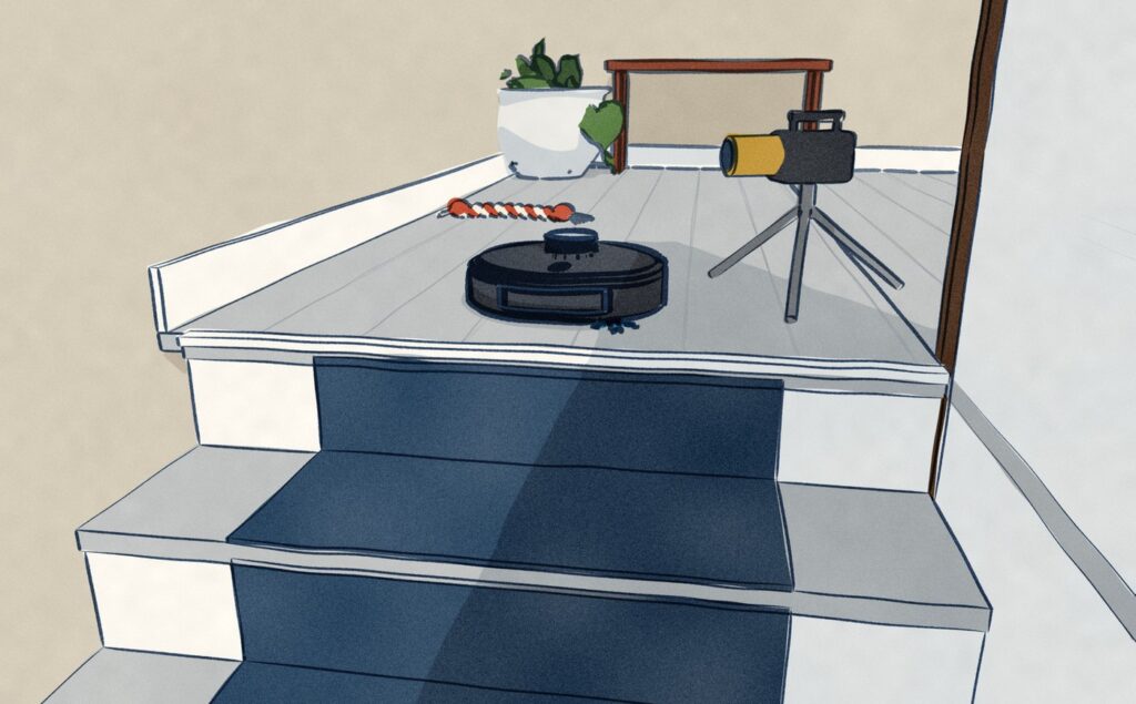 Seen from the stairs below, a robot vacuum waits on the landing a hand's width from the edge of the top step while a small camera on a short tripod films it, with a rope dog toy on the boards behind it.